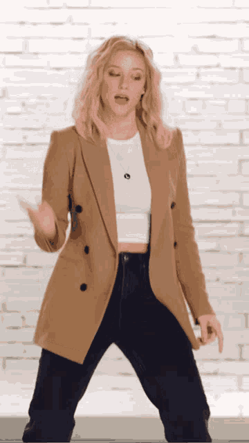a woman in a tan jacket and black jeans is dancing