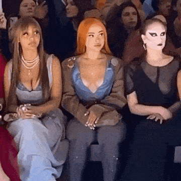 a group of women are sitting next to each other in a crowd at a fashion show .