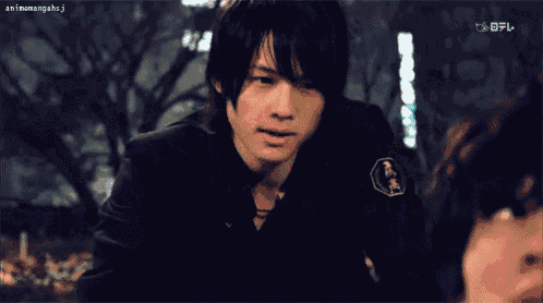 a man in a black jacket with a gold badge on his chest looks at another man