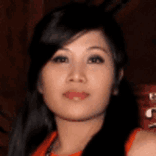 a close up of a woman 's face with long black hair and a red top .