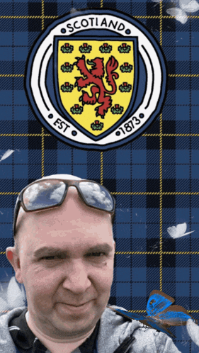 a man wearing sunglasses is standing in front of a scotland crest