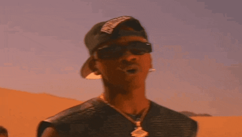 a man wearing a hat and sunglasses is standing in front of sand dunes