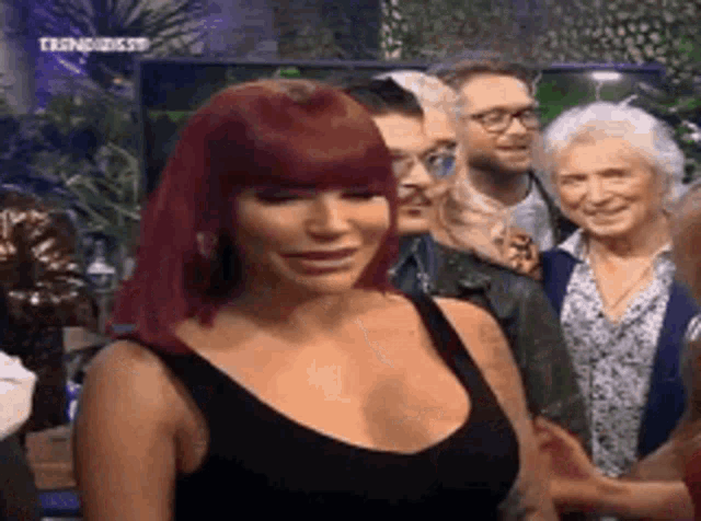 a woman with red hair and a black tank top is smiling in front of a group of people