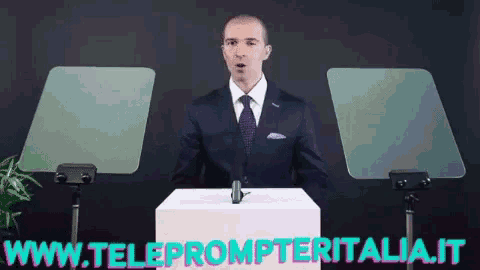 a man in a suit and tie stands behind a podium with the website www.teleprompteritalia.it written below him