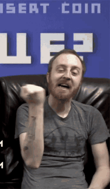 a man with a beard is sitting in front of a blue sign that says insert coin