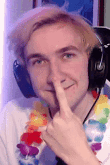 a young man wearing headphones and a lei is holding his finger to his lips .