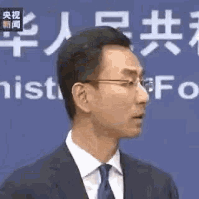 a man in a suit and tie is standing in front of a blue wall with chinese writing on it .