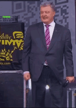 a man in a suit and tie stands in front of a sign that says ally vimtv
