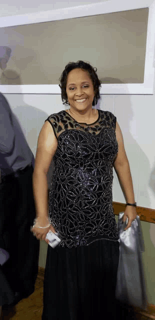 a woman wearing a black dress is smiling and holding a cell phone