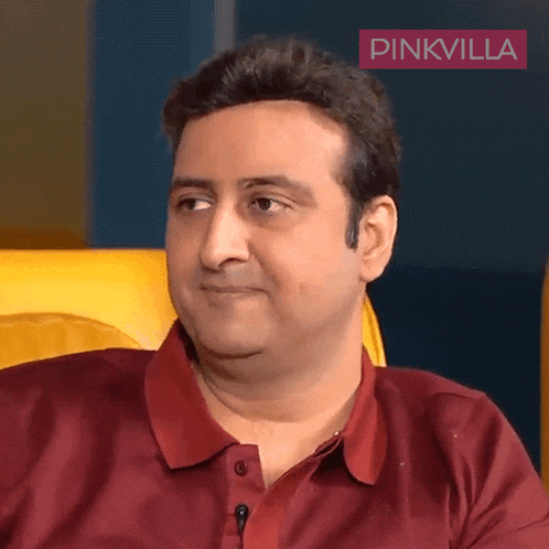 a man wearing a red shirt is sitting in front of a pinkvilla sign