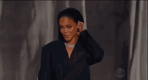 rihanna is wearing a black jacket and a necklace while standing on a stage .