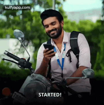a man is sitting on a motorcycle looking at his cell phone and smiling .