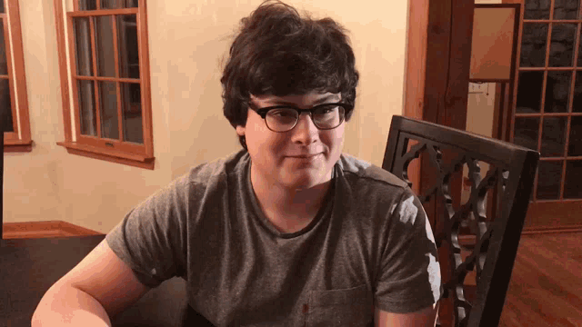 a young man wearing glasses sits at a table in front of a window