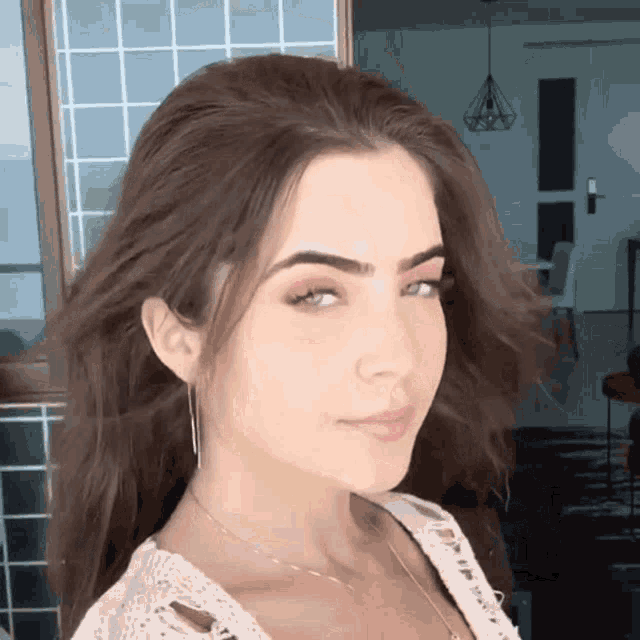 a woman with brown hair and blue eyes is wearing a white top