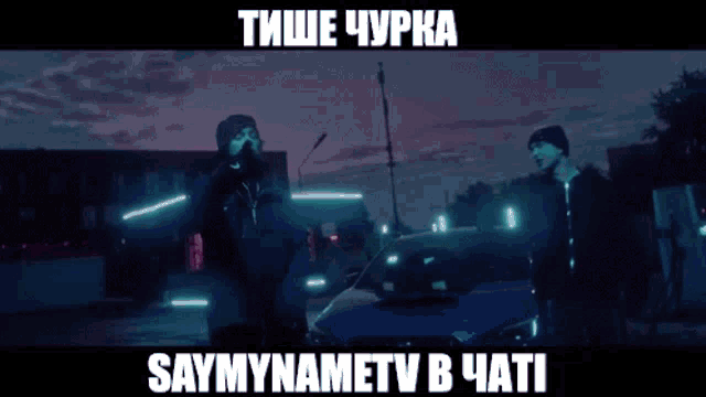 two men are standing in a room with a sign that says saymynametv in a foreign language