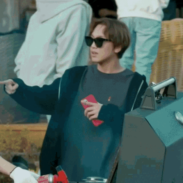 a man wearing sunglasses is standing in front of a grill and holding a bottle of soda .