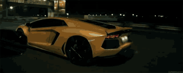 a yellow lamborghini aventador is driving down a street at night .