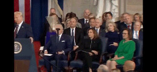 a man in a suit and tie is giving a speech in front of a crowd of people sitting in chairs .