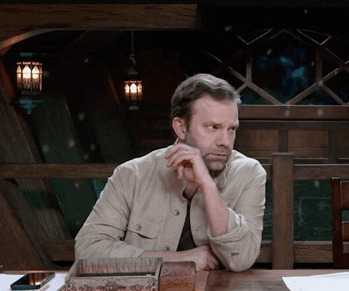 a man with a beard sits at a table with his hand on his chin
