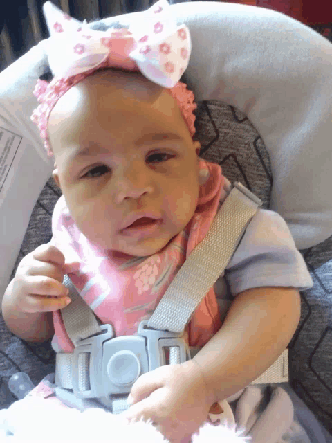 a baby wearing a pink headband and bib is sitting in a bouncer