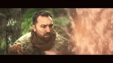 a man is standing in front of a fire in the woods .