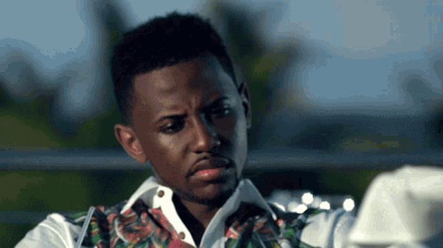 a man wearing a white shirt and a floral vest looks down