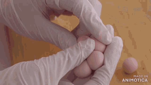 a person wearing white gloves holds a pink ball on a cutting board