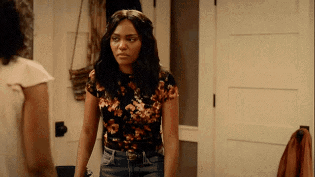 a woman in a floral shirt and jeans is standing in a room with another woman .