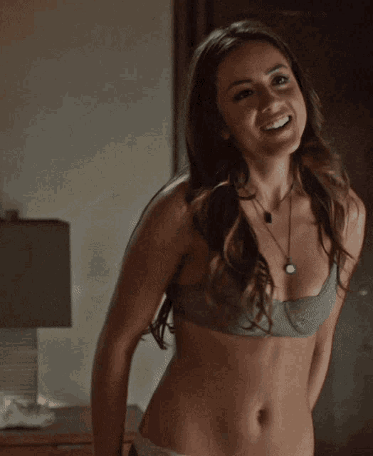 a woman in a bra and underwear is smiling and taking off her pants