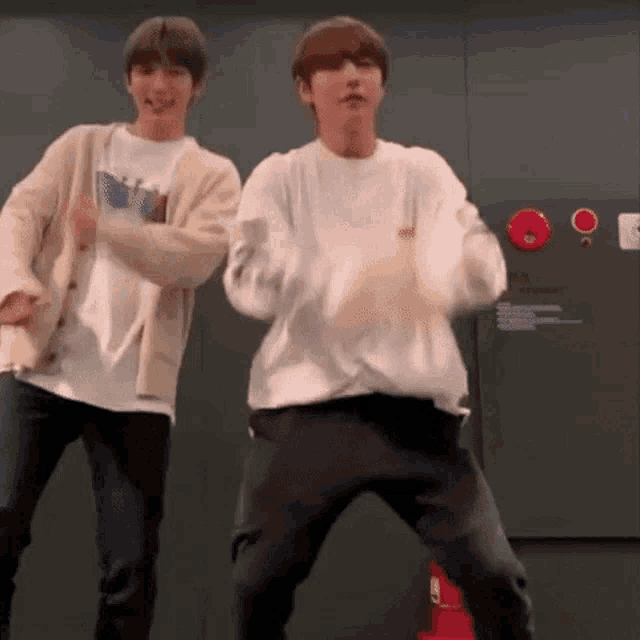 two young men are standing next to each other and dancing in front of a fire extinguisher .