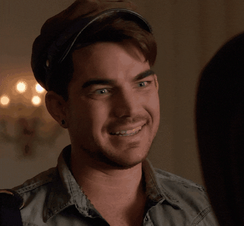 a man wearing a hat and a denim shirt is smiling
