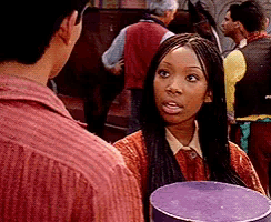 a woman with braids is holding a purple box and talking to a man