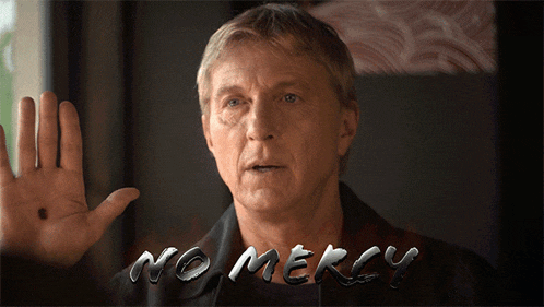 a man holds up his hand in front of a sign that reads no mercy