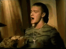 a man wearing a camouflage shirt and a necklace is yawning in a room .