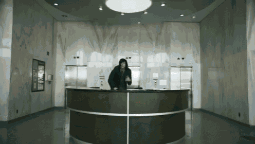 a man in a hooded jacket stands at a reception desk in a lobby