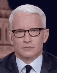 a man in a suit and tie is wearing glasses and making a funny face .