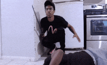 a man in a black shirt with a snake on it is squatting next to a man laying on the floor