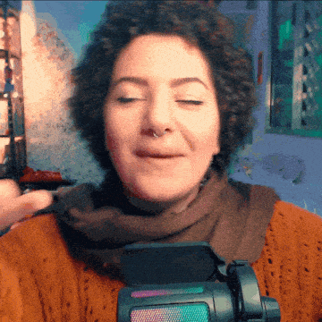 a woman with curly hair and a nose ring is standing in front of a microphone