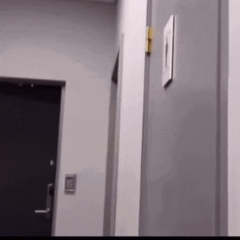 a person is standing in a hallway next to a door and a light switch .