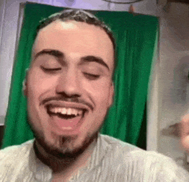 a man with a beard is smiling in front of a green screen .