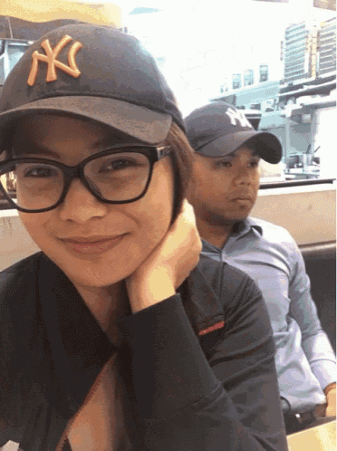 a woman wearing glasses and a ny hat smiles at the camera
