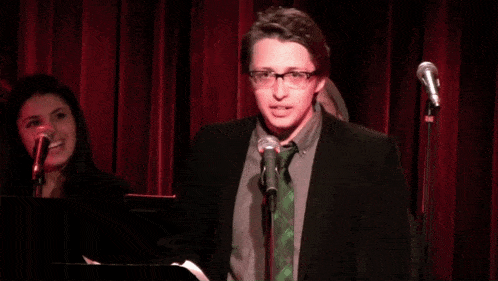 a man in a suit stands in front of a microphone with a green tie