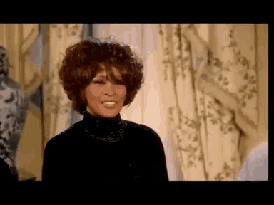 a woman in a black turtleneck is standing in front of a window .