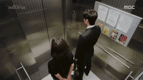 a man and a woman are standing in an elevator that says mbc on the wall