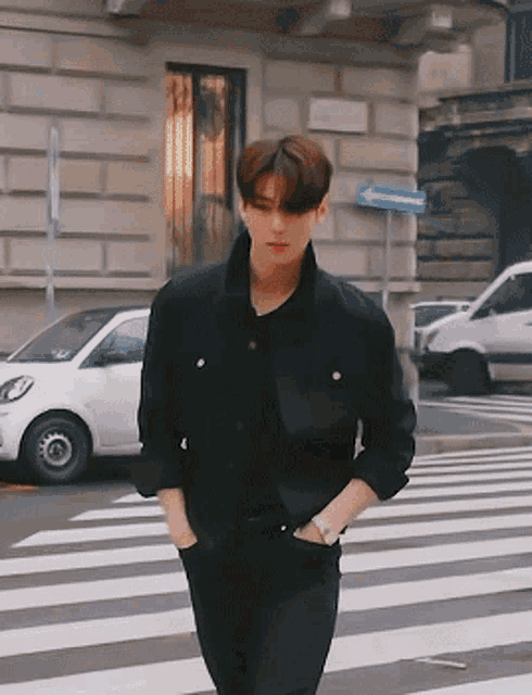 a man in a black jacket is walking across a crosswalk