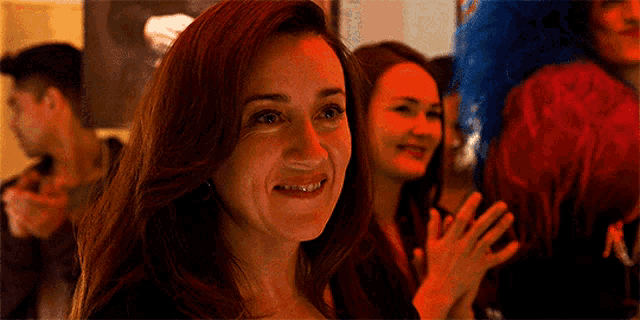 a woman with red hair is smiling in front of a group of people