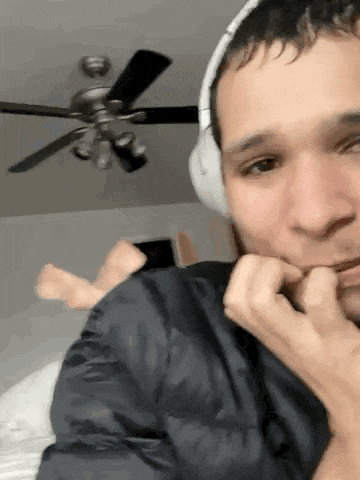 a man wearing headphones is biting his nails while sitting on a bed .