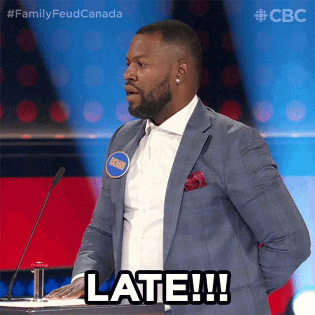 a man in a suit stands in front of a microphone and says late !!!
