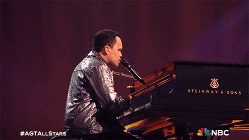 a man is singing into a microphone while playing a steinway piano