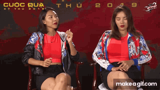 two women are sitting next to each other in front of a sign that says cuoc dua